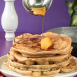 Maple syrup being poured over apple cinnamon pancakes with butter