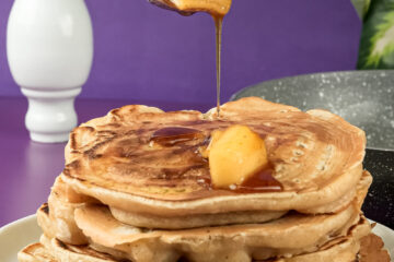 Maple syrup being poured over apple cinnamon pancakes with butter