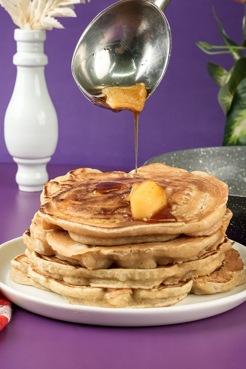 Maple syrup being poured over apple cinnamon pancakes with butter
