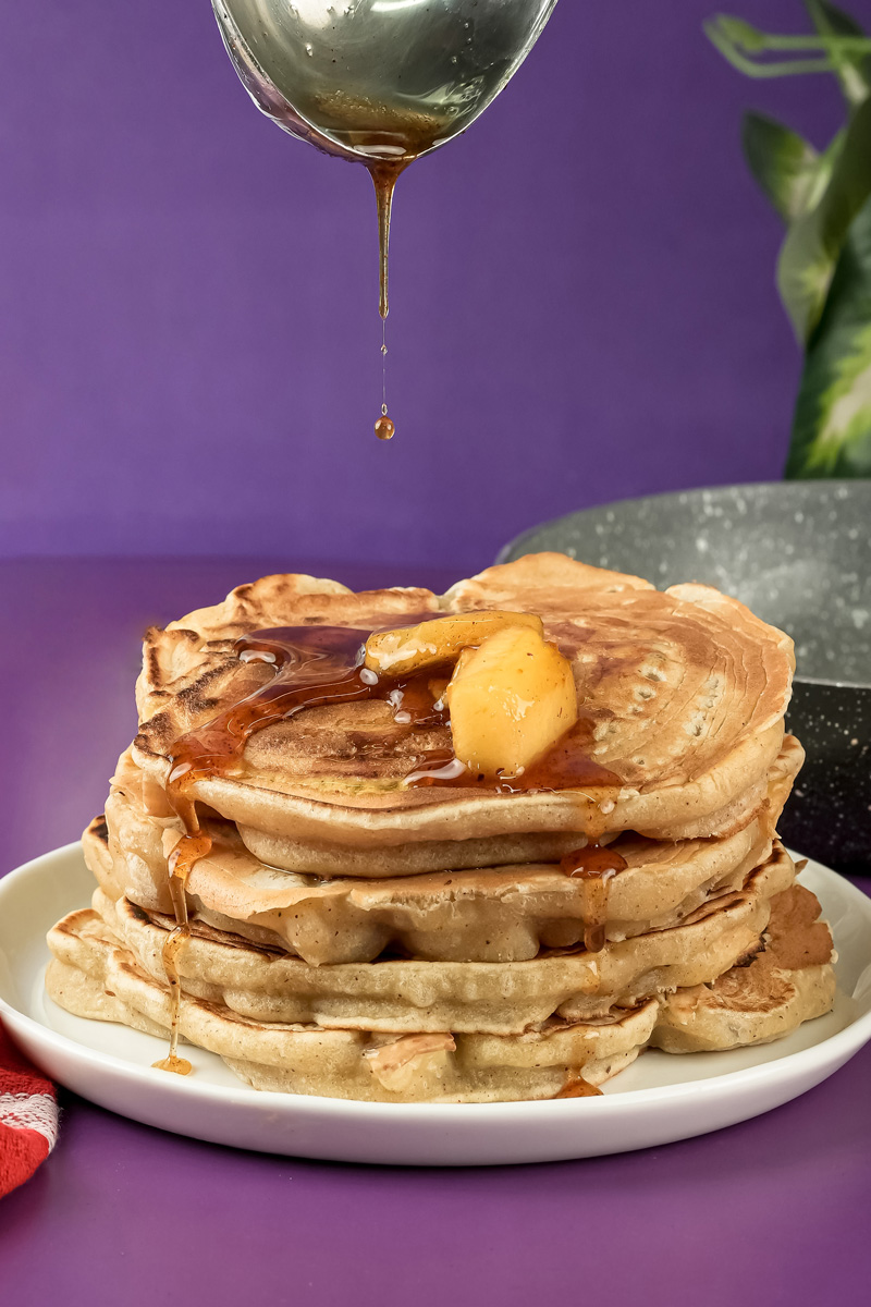 Maple syrup drizzling over apple cinnamon pancakes with apple chunks