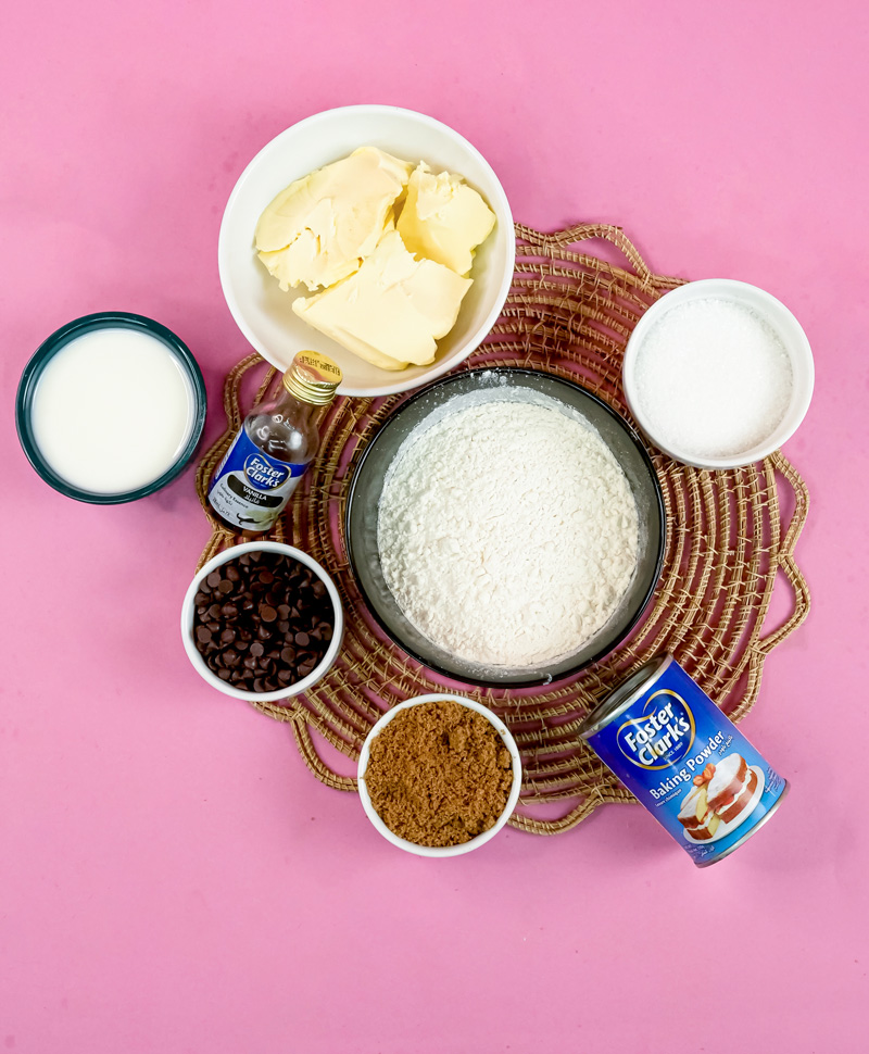 Mini chocolate chip muffin ingredients laid out on pink background with flour, butter, milk, sugar, and chocolate chips