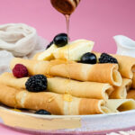 Honey being poured on pancake rolls with berry topping