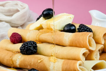 Honey being poured on pancake rolls with berry topping