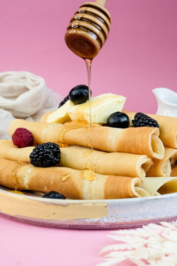 Honey being poured on pancake rolls with berry topping