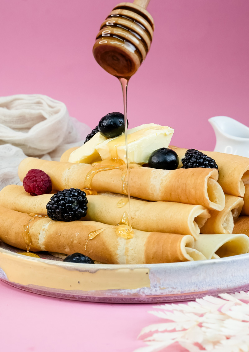 Honey being poured on pancake rolls with berry topping