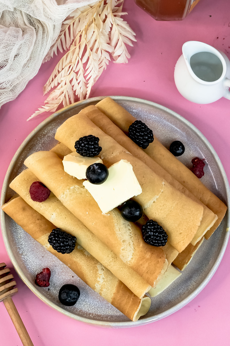 Pancake rolls served with fresh berries and butter on plate