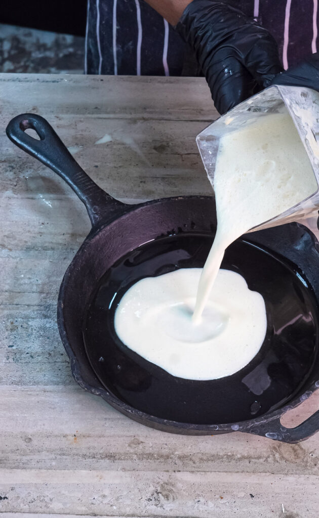 Pouring Dutch baby batter into buttered cast iron skillet