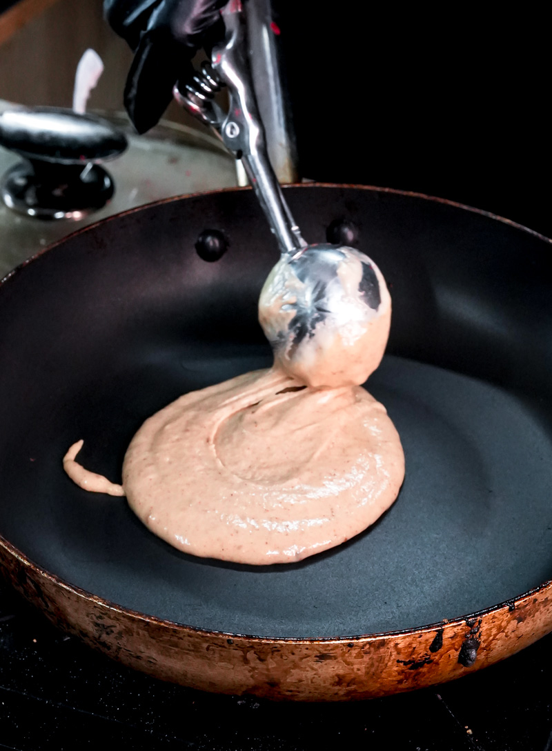 Pouring peanut butter pancake batter onto hot griddle with ladle