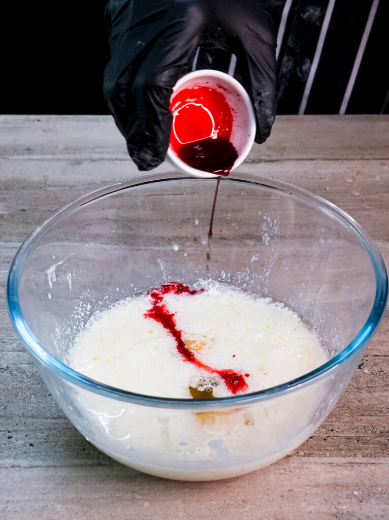 Pouring red food coloring into pancake batter mixture