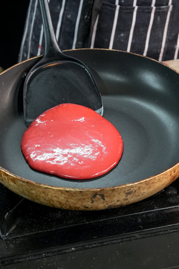 Red velvet pancake batter cooking in skillet