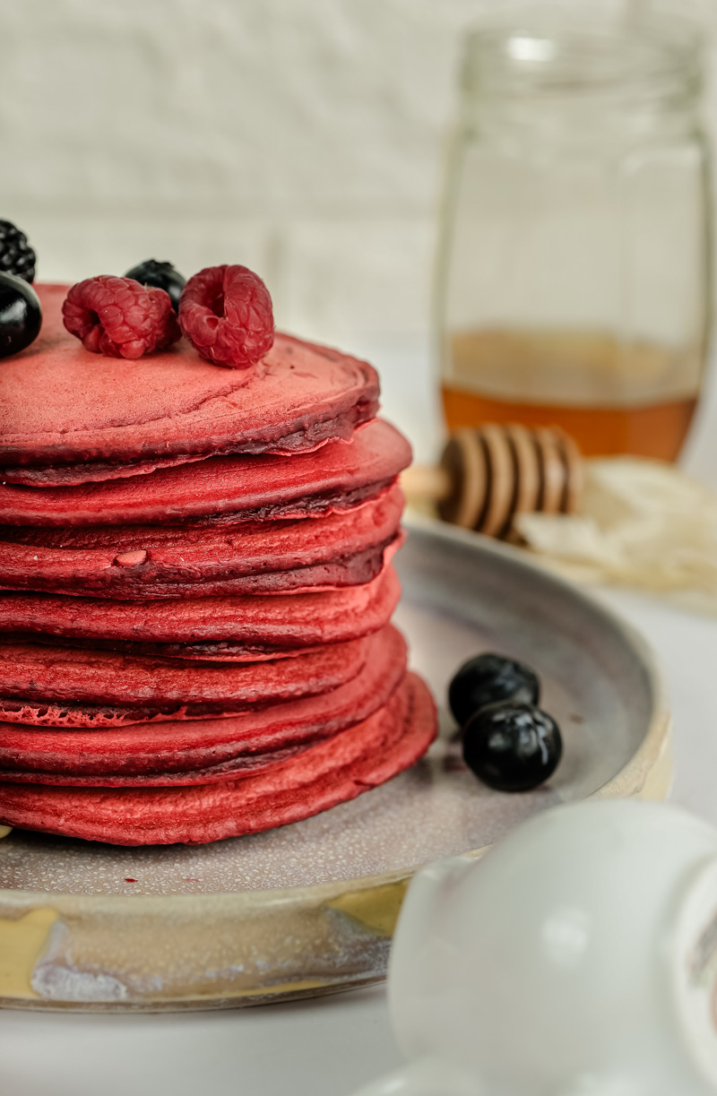 Red velvet pancake stack with honey in background