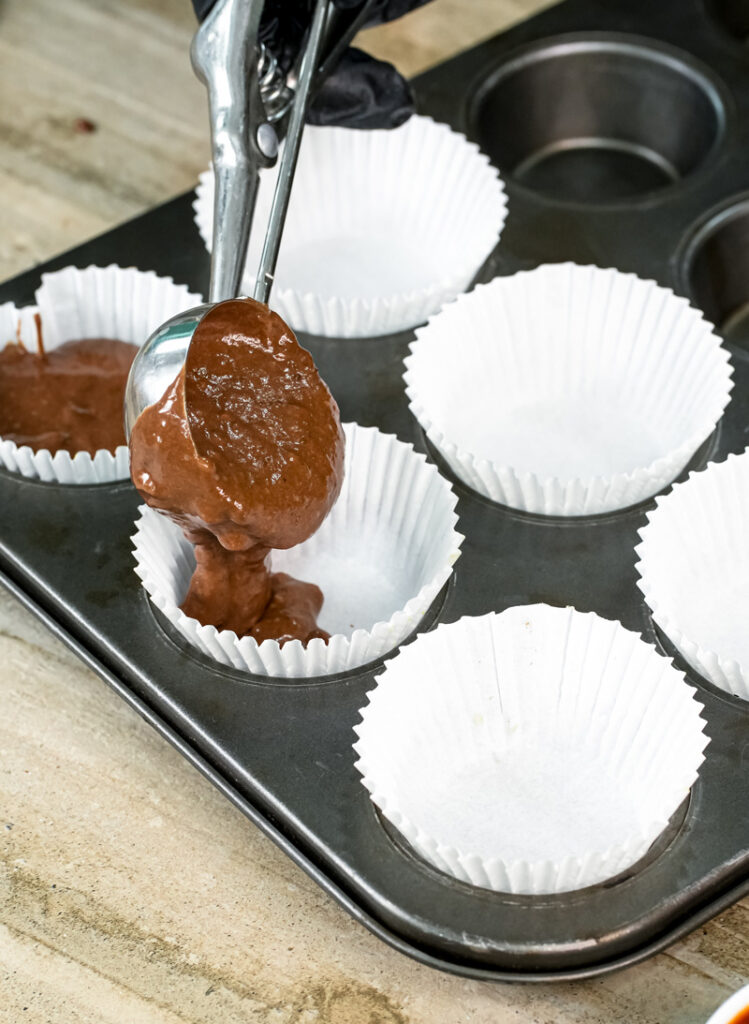 Scooping chocolate muffin batter into lined muffin tin