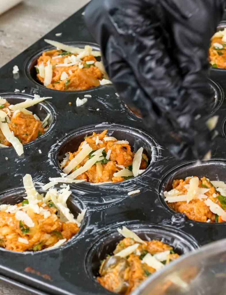 Sprinkling extra cheese on top of pizza muffins before baking