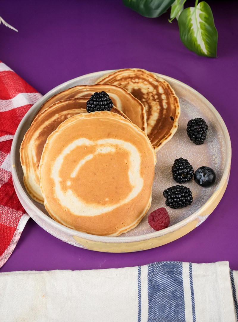 Stack of fluffy silver dollar pancakes garnished with mixed berries on white plate