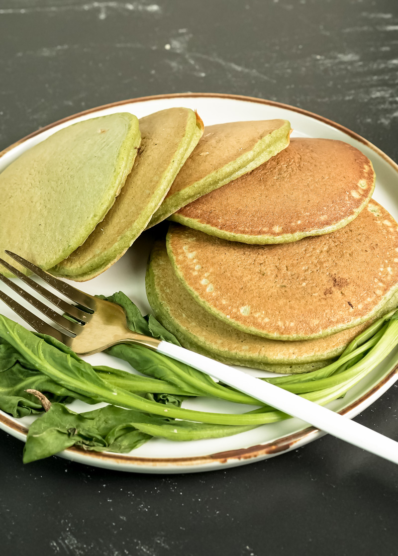Stack of green banana spinach pancakes with fresh spinach garnish