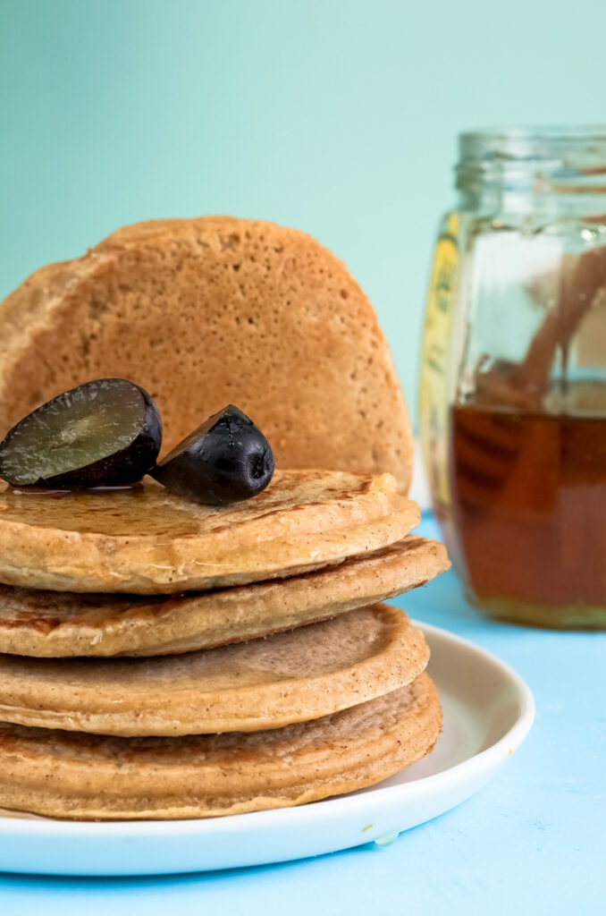 Tall stack of oat pancakes with honey jar and dates