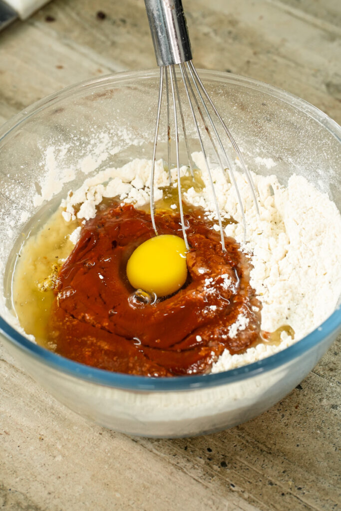 Adding egg to pizza muffin batter with whisk